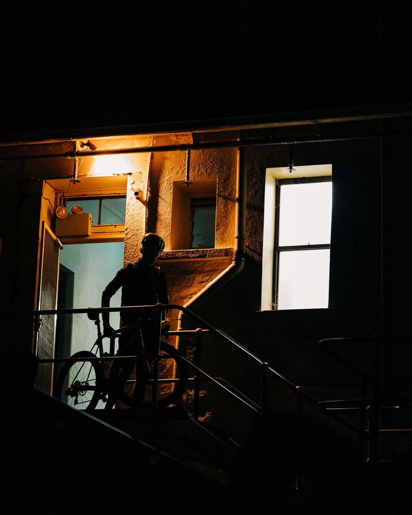 Matt Bird wheeling his bike down exterior stairs in the dark.