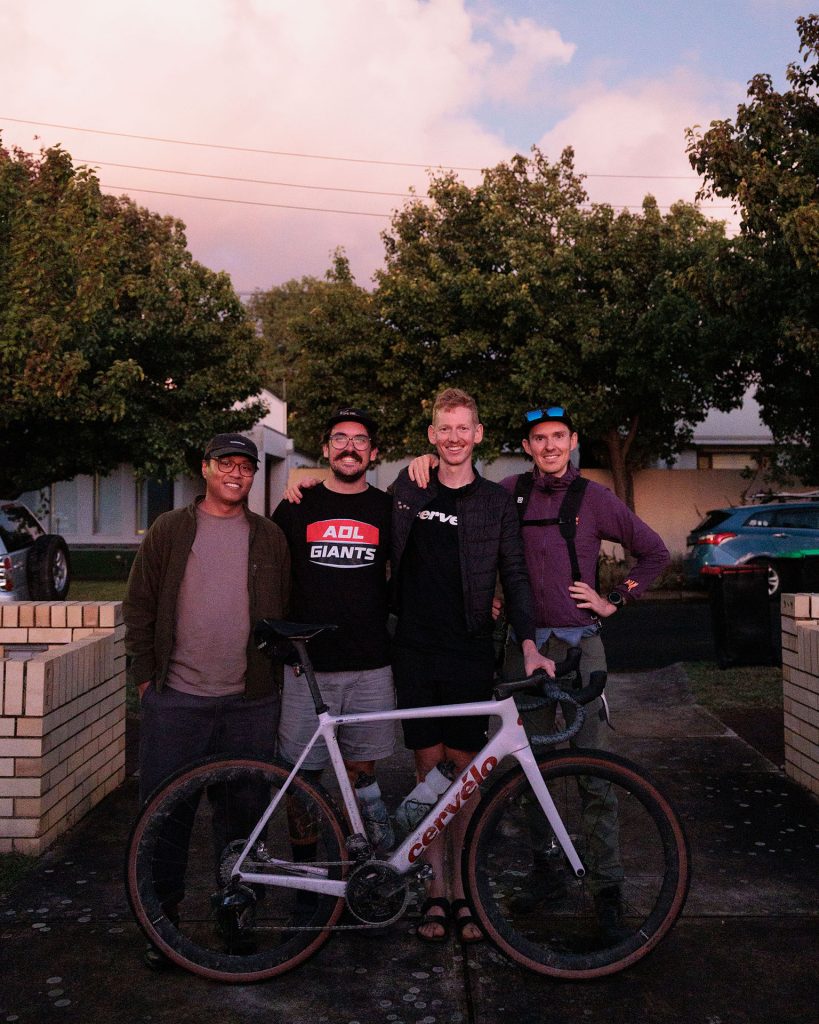 Four people standing together behind a bike, smiling towards the camera.